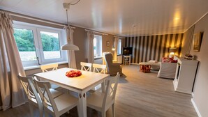 A modern hotel room with a dining area, a living room, and a TV. - Captains Lodge - Bathtub, Shower, Terrace, Grill, Secluded & Close to the Beach (Steinbergkirche)