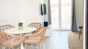Un comedor con una mesa redonda y sillas de mimbre, una lámpara colgante y vistas a un balcón con cortinas.