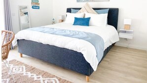 Un dormitorio con cama, silla, mesita de noche, espejo y un cuadro en la pared.