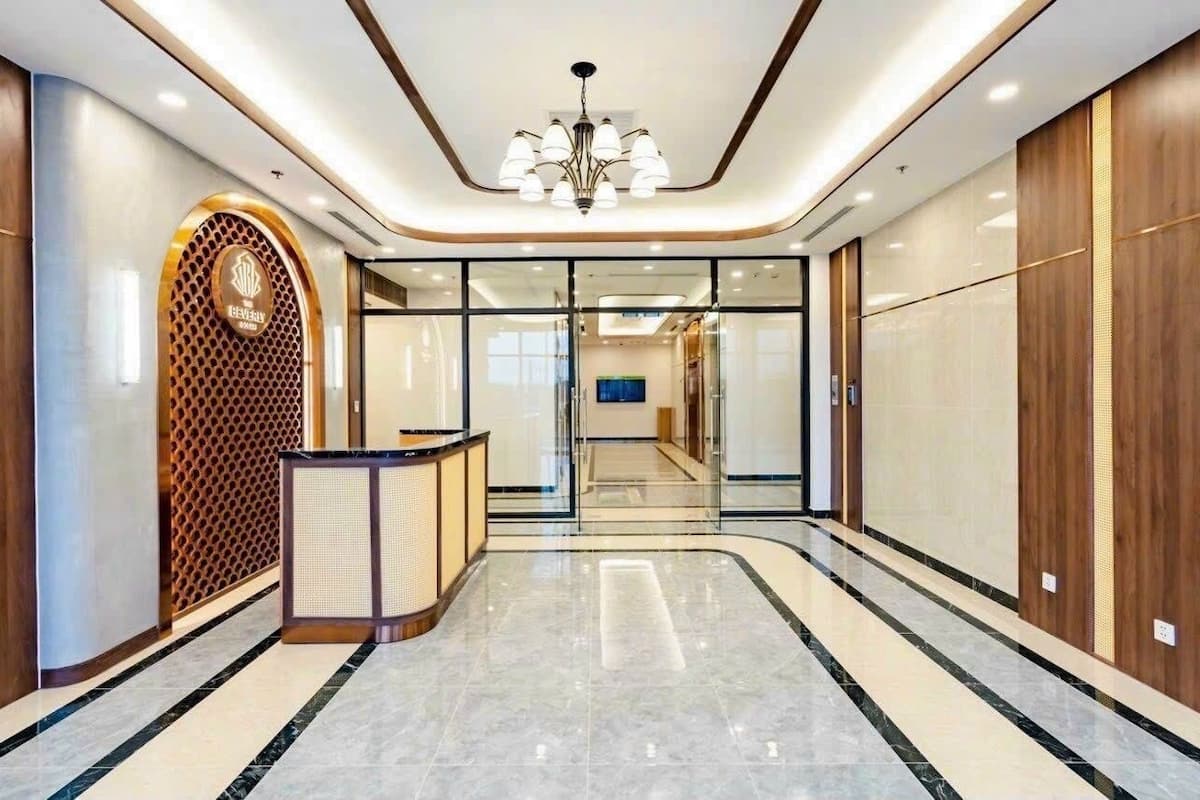 Un hall d’hôtel moderne, avec un comptoir d’accueil, un lustre et une cloison en verre donnant accès à un autre espace.