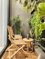 Varanda com cadeira e mesa de bambu, cercada por diversos vasos de plantas.