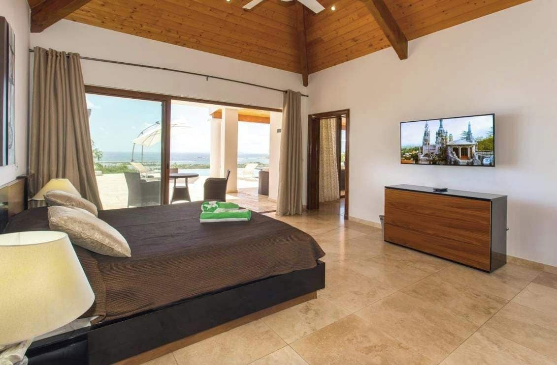 A bedroom with a bed, a TV, a wooden dresser, and a view of the outdoors.