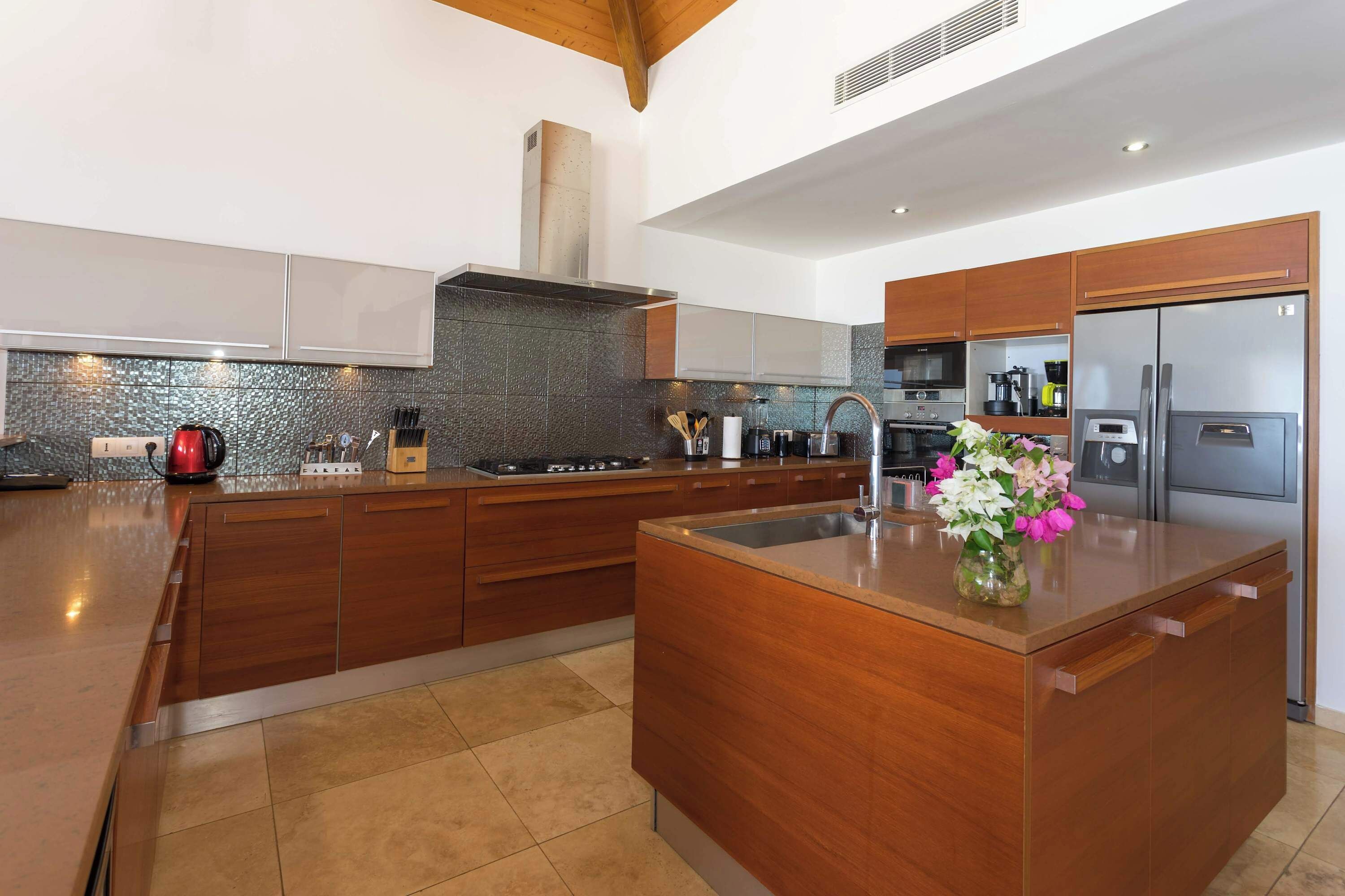 Una cocina moderna con armarios de madera, una isla central, electrodomésticos de acero inoxidable y un jarrón decorativo.