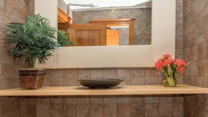 Une salle de bain avec un miroir, un lavabo, une plante en pot et un vase rempli de fleurs.