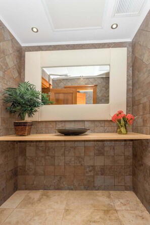 Un bagno con uno specchio, un lavandino, una pianta in vaso e un vaso con fiori.