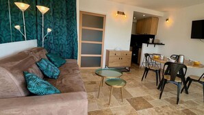 A modern living room with a brown sofa, teal patterned curtains, and a dining area with a wooden table and chairs.