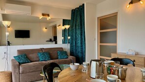 A modern living room with a brown sofa, teal cushions, a wooden dining table with various items, and a large mirror.