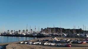A marina with numerous boats docked along the shoreline, surrounded by palm trees and buildings in the background.