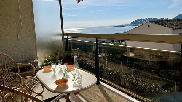 A balcony with a table set for dining, overlooking a coastal view with buildings and a clear sky.