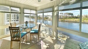 Ein Wintergarten mit Glastisch und -stühlen, Deckenventilator und Blick auf ein Gewässer.