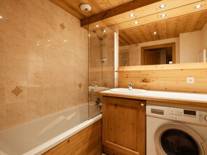 Ett badrum med badkar, en dusch med glasväggar, ett handfat med underskåp i trä och en tvättmaskin.