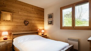 Une chambre à coucher aux murs lambrissés, avec un lit, des lampes de chevet, un radiateur et une fenêtre donnant sur des arbres.