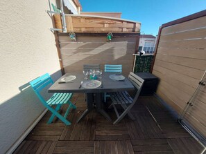 Pátio com mesa posta para quatro, rodeado por cadeiras de madeira e um cercado de madeira.