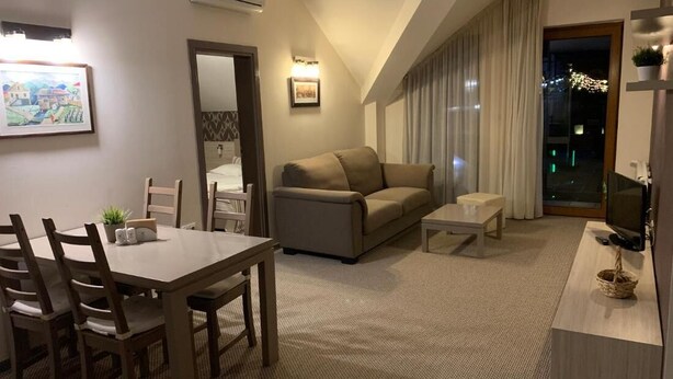 A modern living room with a sofa, a dining table with chairs, a TV, and a balcony with curtains. - Stayinn Granat - 2 Bedroom Apartment - Next to Gondola Lift, Perfect for 4pers (Bansko)