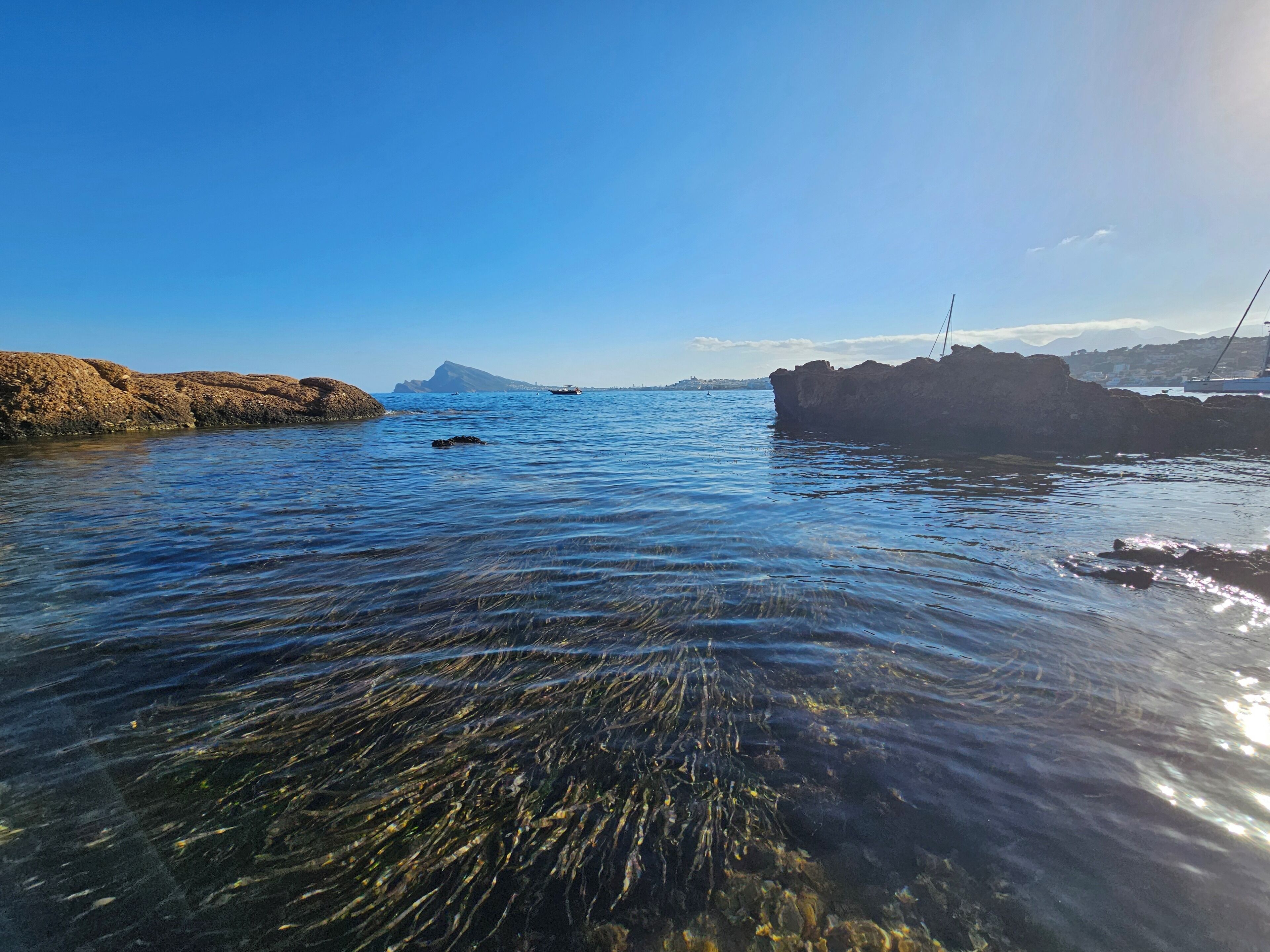 A coastal scene with clear water, rocky formations, and distant mountains.