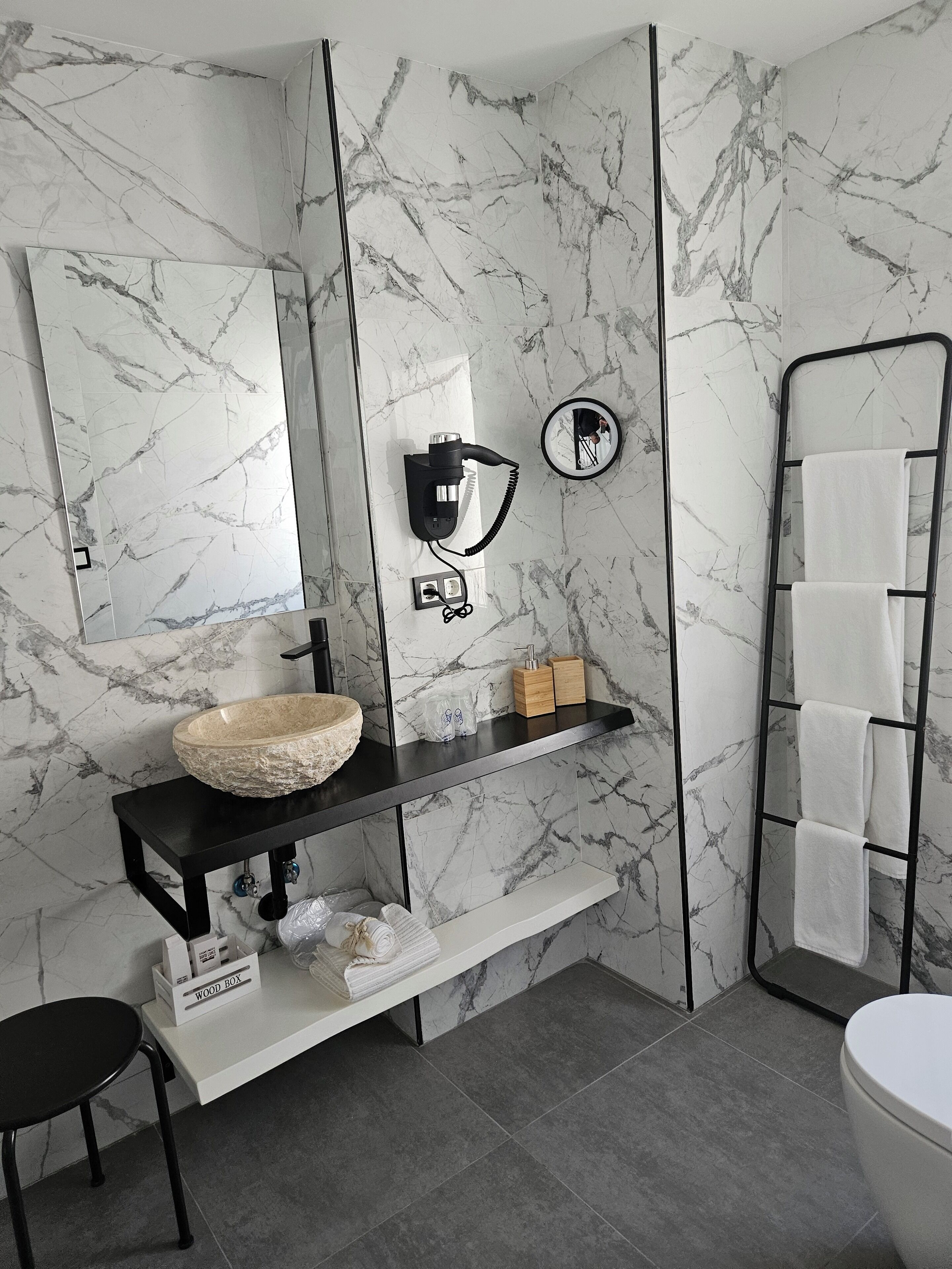 A modern bathroom with a marble backsplash, a black vanity with a stone sink, a towel rack, and a mirror.