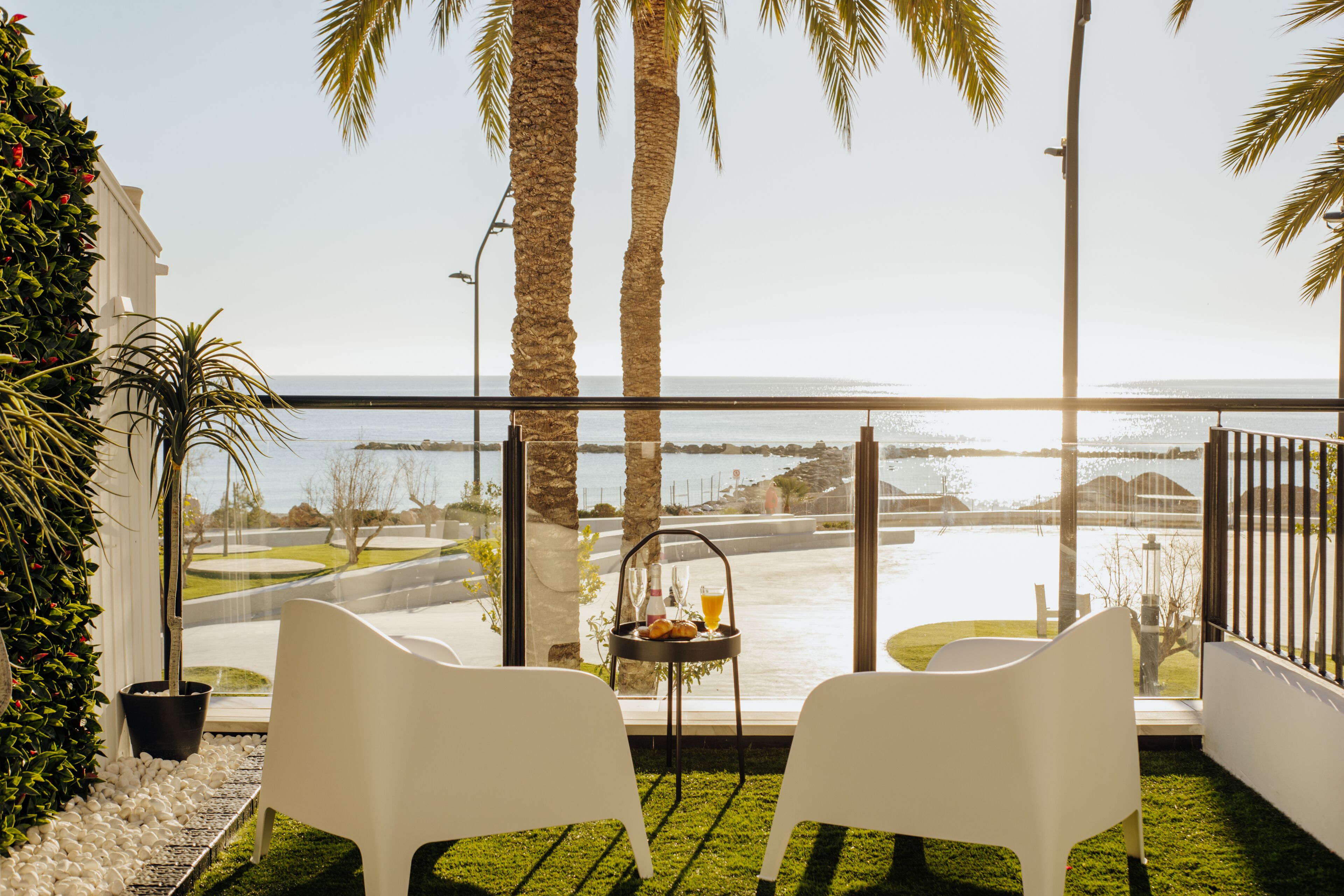 A balcony with two white chairs, a small table with a bottle and a glass, and a view of the sea.