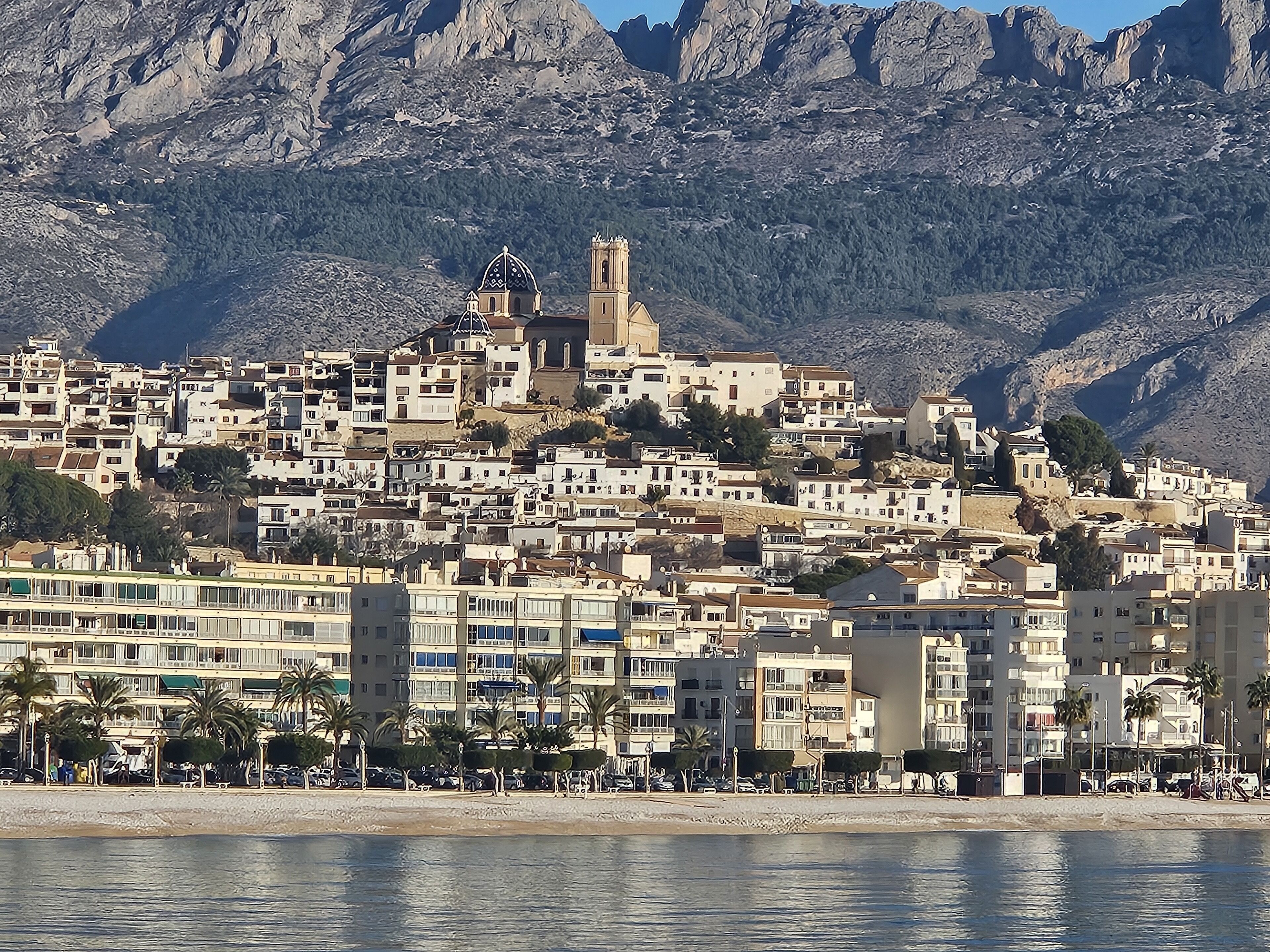 Un pueblo costero con una iglesia destacada y una montaña rocosa al fondo.