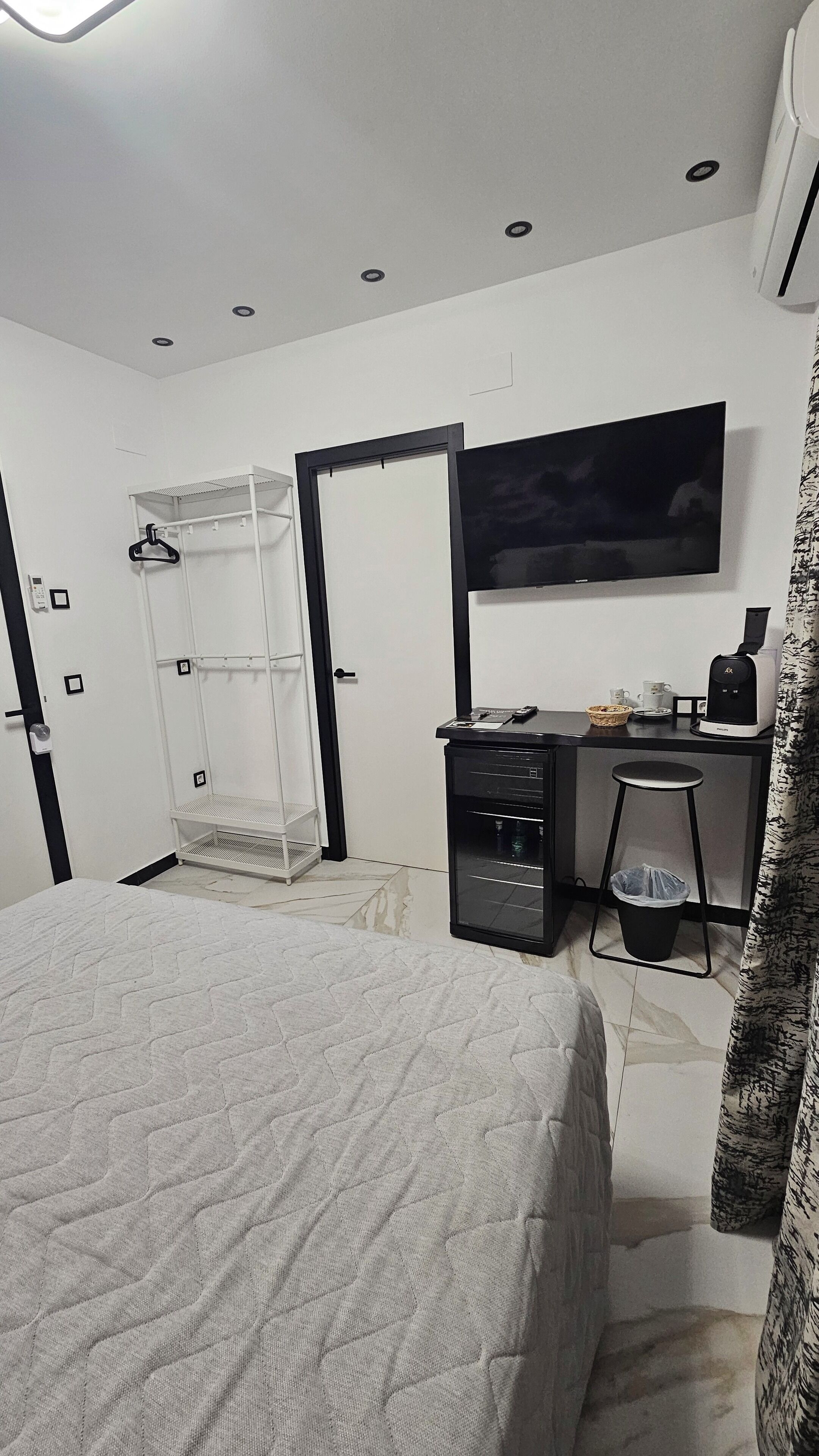 A hotel room with a bed, a desk with a chair, a TV, a coffee machine, and a wardrobe.