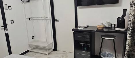 A hotel room with a bed, a desk with a chair, a TV, a coffee machine, and a wardrobe.