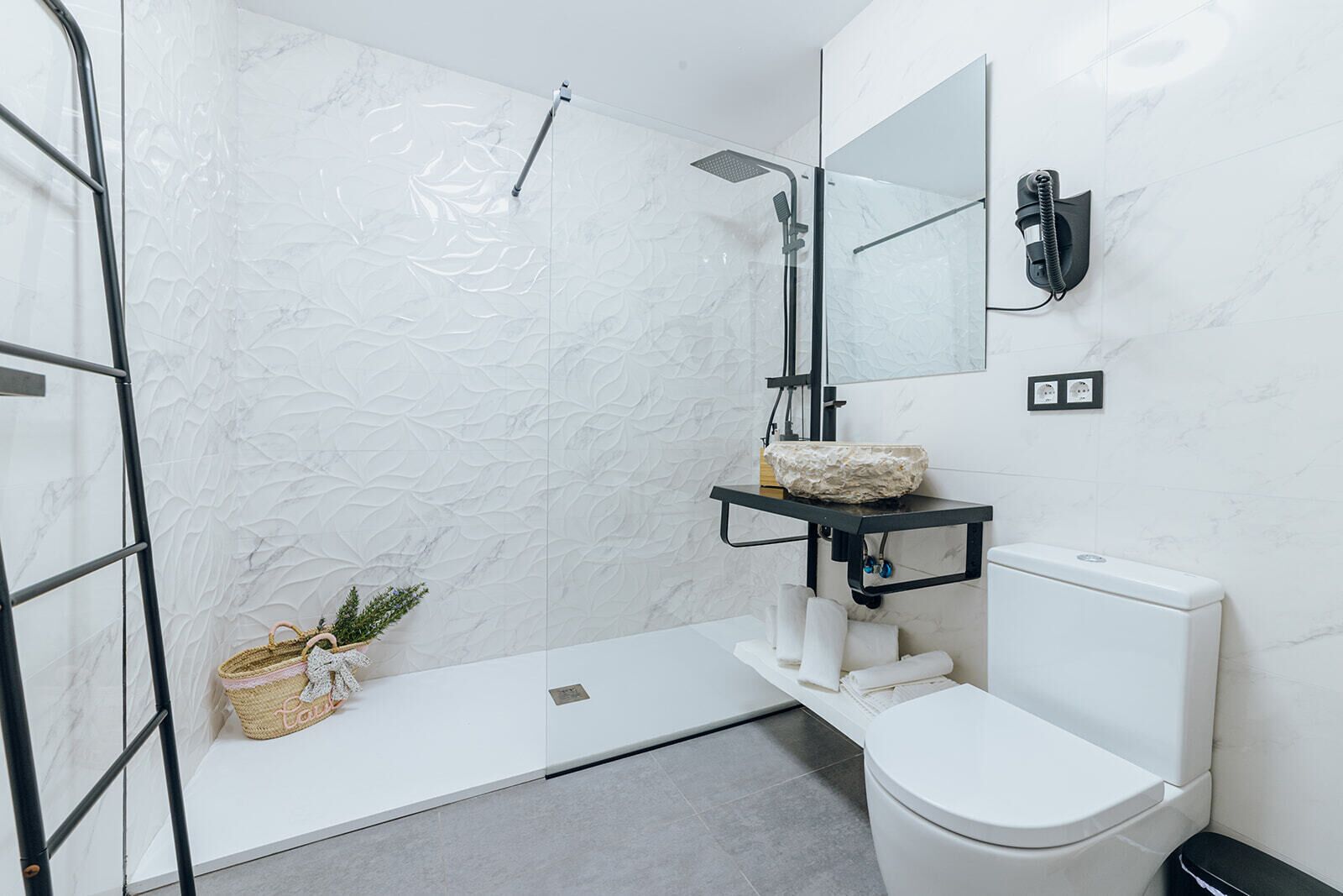 A modern bathroom with a glass shower enclosure, a white toilet, a marble-patterned wall, and a small shelf with a decorative item.
