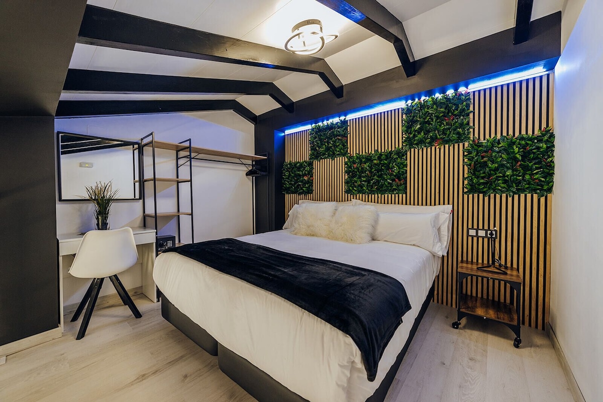 A modern bedroom with a bed, a desk, and a chair. There is a wooden slat wall with green plants.