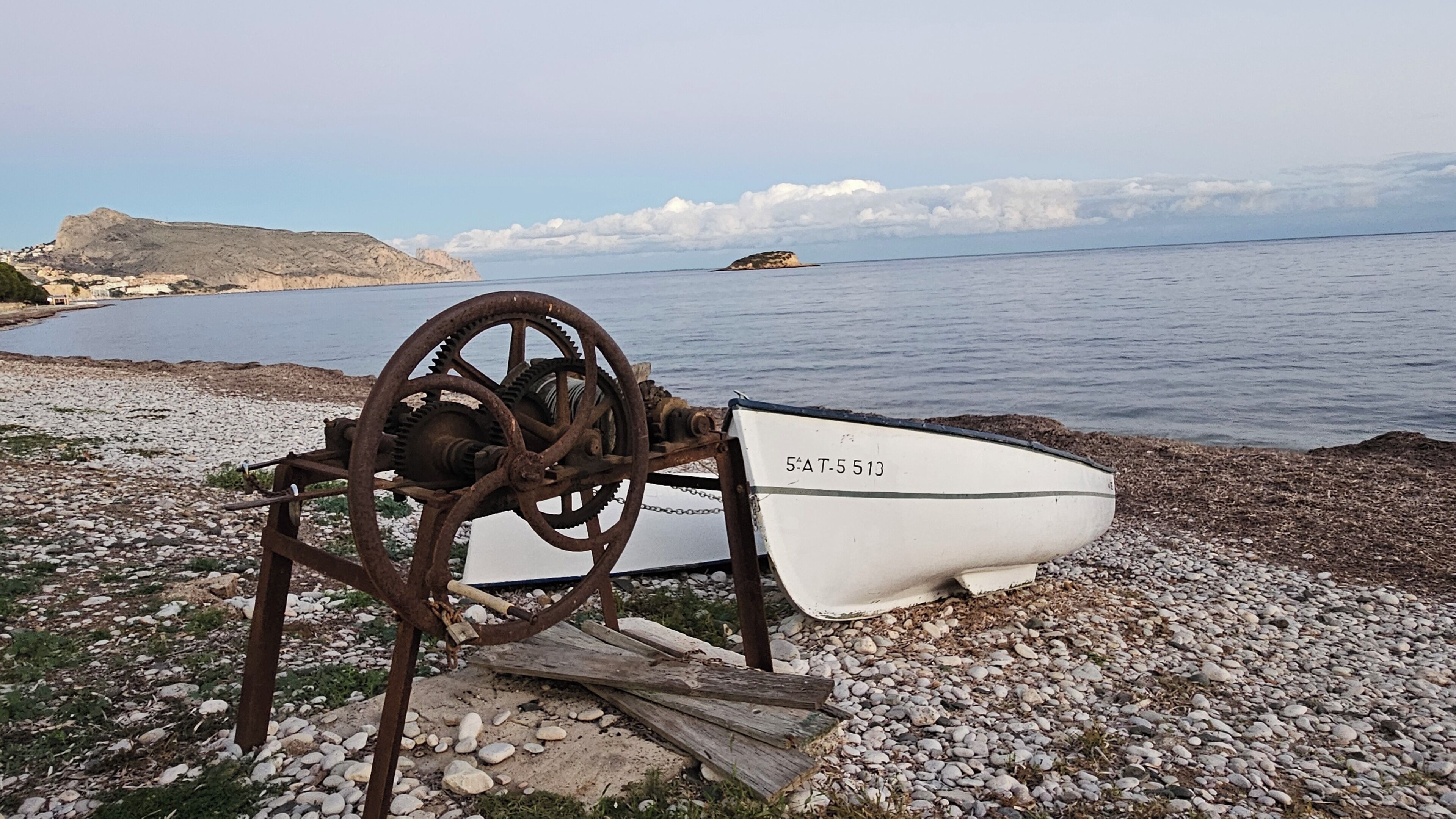 A boat with the number 5-AT-5 513 on a rocky shore by the sea.