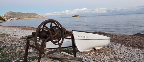 A boat with the number 5-AT-5 513 on a rocky shore by the sea.