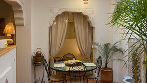 A dining area with a table set for four, surrounded by chairs, a decorative arch, and a potted plant.