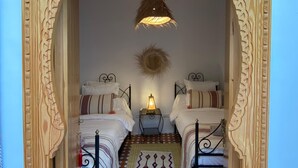 A room with two beds, a patterned rug, and a hanging light fixture.