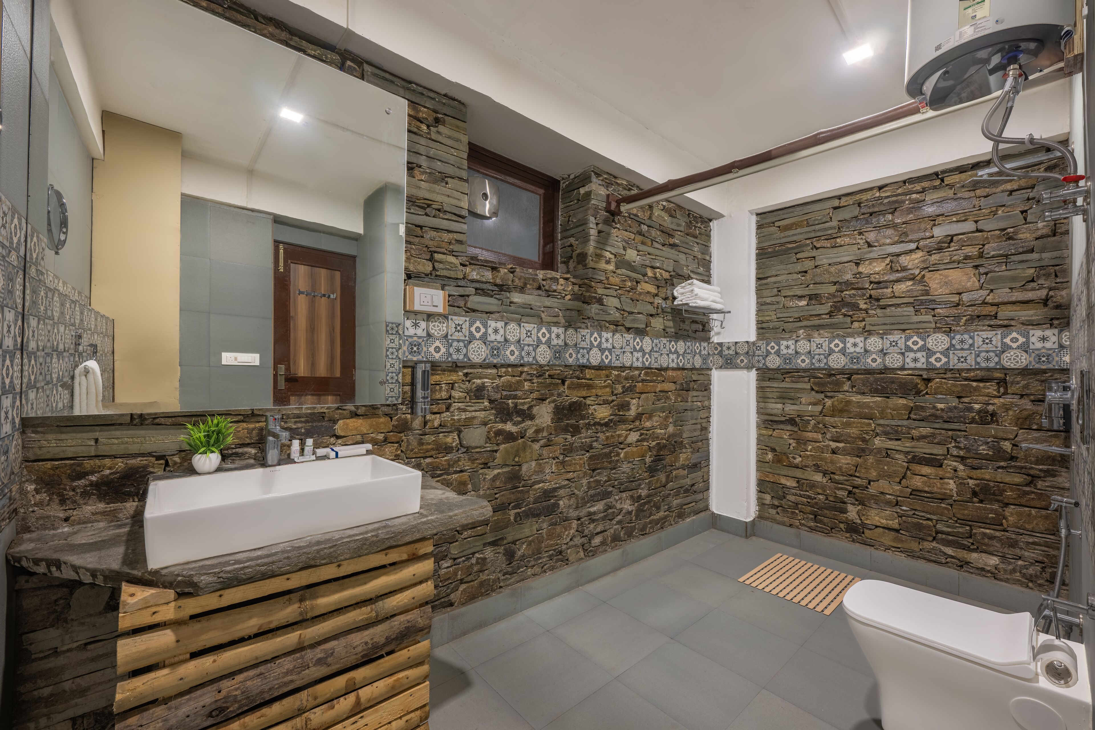 A bathroom with a stone wall, a wooden vanity, a white sink, and a shower area.