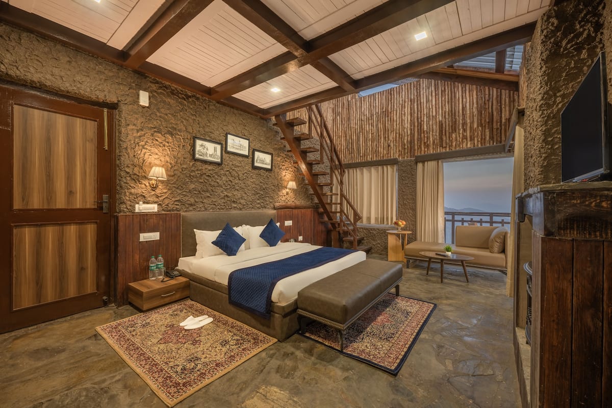 A bedroom with a large bed, wooden walls, a stone floor, a staircase, and a balcony with a view.