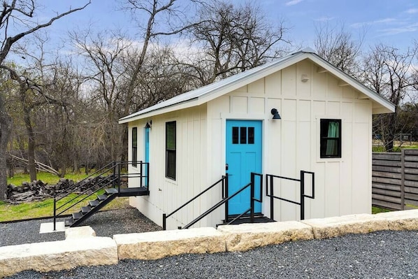Un petit bâtiment d’un seul étage, avec une porte bleue, un escalier menant à l’entrée et une zone environnante recouverte de gravier.