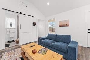 A modern living room with a blue sofa, a wooden coffee table, and a door with a towel rack. - Casita Fulton - Fire Pit & Close to Main St (Fredericksburg)