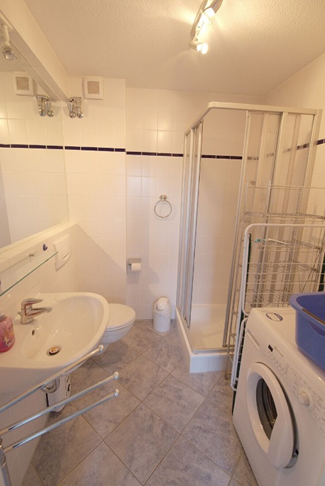 A bathroom with a shower, toilet, sink, and washing machine.