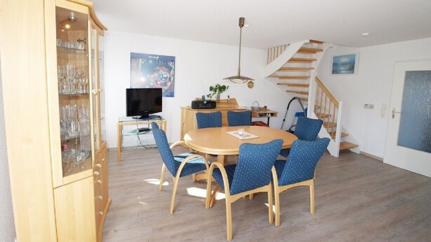 A dining area with a round table, blue chairs, and a wooden cabinet with glass doors.