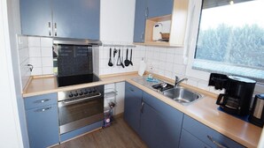 A compact kitchen with blue cabinets, a stainless steel stove, and a window overlooking a forest.