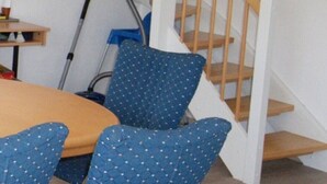 A staircase with wooden steps and white railings, a dining table with chairs, and a vacuum cleaner in the corner.