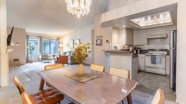 Eine moderne Küche mit Einbauofen und Kühlschrank, ein Essbereich mit großem Tisch und Stühlen sowie ein Wohnzimmer mit Sofa und Couchtisch.