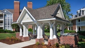A gazebo with a brick base and white pillars, surrounded by a landscaped garden with mulch and small plants.