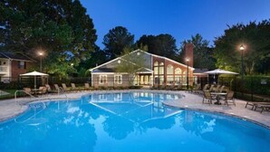 A swimming pool with lounge chairs and umbrellas, surrounded by a building with large windows and a brick facade. - City Chic: 1BR Gem Perfect for Couple (Hampton)