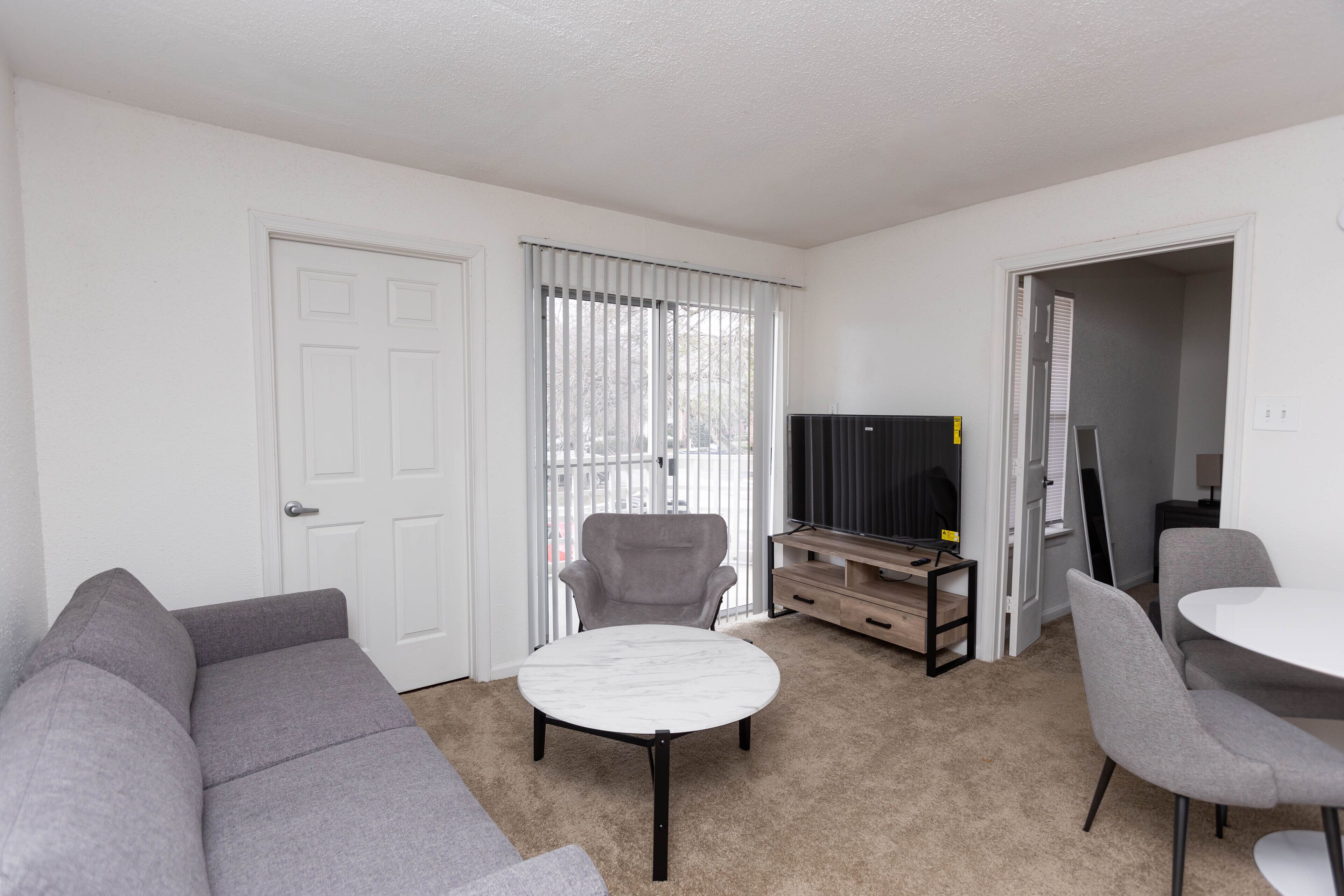 A living room with a grey sofa, a round coffee table, a TV stand, and a dining table with chairs.