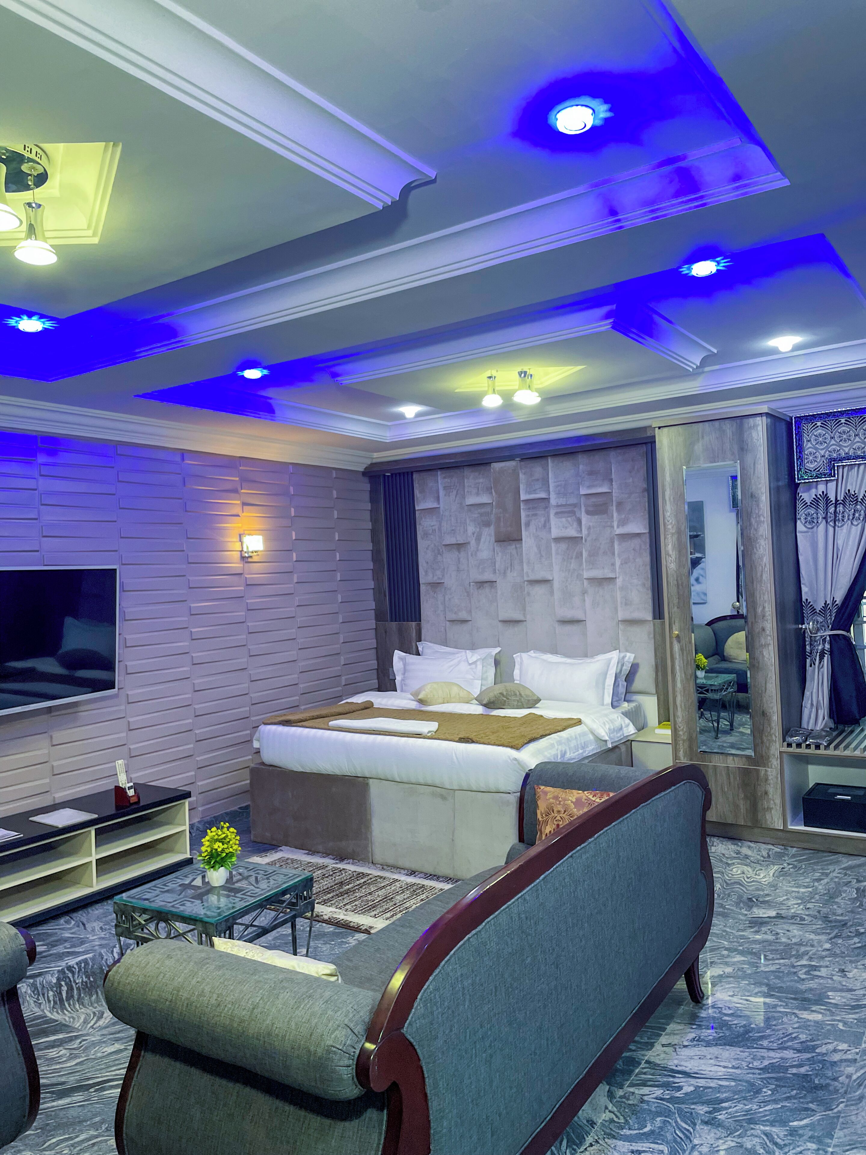 A modern bedroom with a bed, a sofa, a TV, and a mirror.