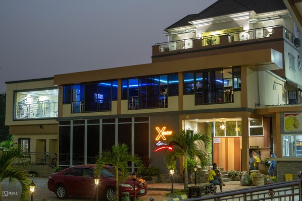 A two-story hotel with a neon sign, large windows, and a red car parked in front. - Dfranklin Apartment and Event Centre (Abuja)