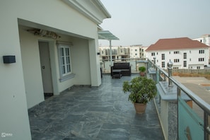 A balcony with a stone floor, a potted plant, and a seating area with a table and chairs.