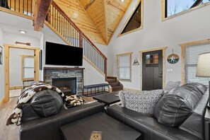 Una sala de estar moderna con chimenea de piedra, sofá de cuero y una escalera de madera.