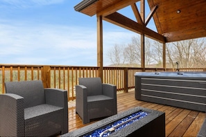 A wooden deck with two wicker chairs, a built-in hot tub, and a fire feature.