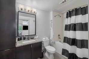 Een moderne badkamer met een donker houten wastafelmeubel, een wit toilet en een zwart-wit gestreept douchegordijn.