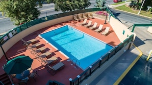 Ein Pool auf dem Dach mit Liegestühlen und Sonnenschirmen, umgeben von einem grünen Zaun.