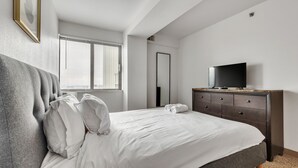 Ein Schlafzimmer mit einem Bett, einem Schminktisch, einem Fernseher und einem Fenster mit Jalousien.